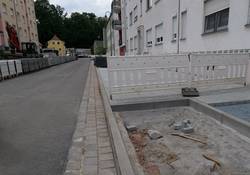 Neu betonierte Straße neben Bauzaun und Baumquartier, noch ohne Substrat.