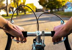 Hände greifen an Fahrradlenker vor Hintergrund Straße mit Baumen und Himmel