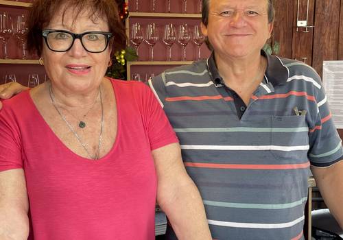 Frau und Mann lächelnd mit Weingläsern im Hintergrund