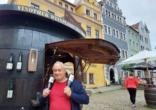 Mann steht vor Weinfass und hält zwei Flaschen